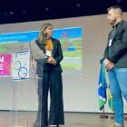 Homem e mulher em palco se olham, no telão aparece o nome de Joinville