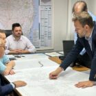 Prefeito aponta para mapa em mesa com outras autoridades em volta