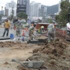 Homens de uniforme e capacete trabalham em obra de recuperação de rua