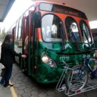 Imagem de um ônibus verde na parte de baixo e laranja na parte de cima, com bicicletas acopladas na frente e janelas arrendondadas