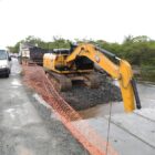 Máquina trabalha na construção de travessia com pré-moldado e carro passa ao lado em pista liberada