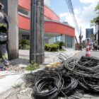 Fios não utilizados enrolados no chão depois de serem retirados de poste, homem com capacete e uniforme ao lado de escada trabalha na remoção