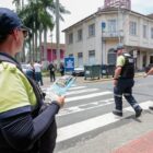 Agente de trânsito atravessa na faixa de pedestre ao lado de um homem enquanto outra agente de trânsito observa