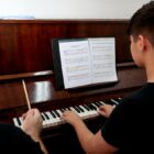 Aluno toca piano ao lado de professor