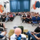 Prefeito, vice, secretário e palestrantes sentados na frente de sala e plateia com alunos observam