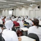 Merendeiras de touca e uniforme estão sentadas e olhando para palestrante