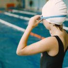 Criança com touca e óculos de natação em frente a uma piscina