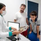 Pai e filho em sala de vacinação são atendidos por enfermeira em frente a computador