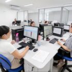 Pessoas sentadas em cadeiras, usam computadores em local de trabalho