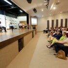 Quatro pessoas sentadas em cadeiras em palco em frente a plateia