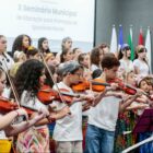 Alunos tocam violinos vestidos com uniformes e peças da cultura afro