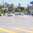 Imagem de rua, em esquina, com sinalização viária e carros trafegando ao fundo