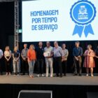 Servidor recebe certificado em cima do palco, com prefeito e secretários