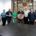 Prefeito segura placa redonda ao lado de homens e mulheres e posam para foto