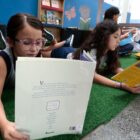 Alunos deitados em tapete no chão de sala de aula leem livros