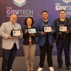 Cinco pessoas posam para foto segurando uma placa de premiação