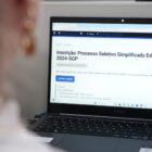 uma pessoa está na frente do computador e na tela está a aberta a página da prefeitura com o Edital do Processo Seletivo