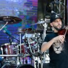 Homem toca violino em palco, atrás um baterista toca o instrumento