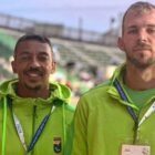 Dois homens, um moreno e um loiro, com uniforme verde claro, posam para foto