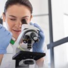 Mulher com luvas observa algo em microscópio