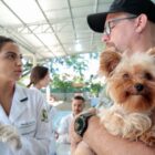 Homem segura cãozinho no colo e fala com profissional com jaleco branco