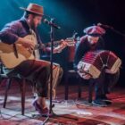 Dois músicos se apresentam em palco, um com violão e outro com sanfona
