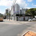 Imagem de um cruzamento de ruas, com comércios e uma obra na pista em andamento