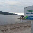 Imagem de uma praia com placa na areia escrito própria para banho