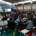 Participantes do curso de formação ouvem sentados em um ginásio as instruções do secretário de educação