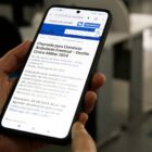 Pessoa segura celular nas mãos e na tela está a página do site da Prefeitura com as informações as inscrições para comércio ambulante no Desfile da Independência