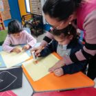 Professora auxilia duas alunas em sala de aula
