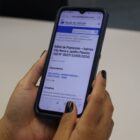 Mão feminina segura celular que está na página do edital