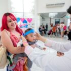 Mãe segura filho no colo e profissional da saúde interage com a criança