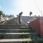 Homem com equipamentos de proteção utiliza cortador de grama em escadas de cemitério