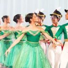Bailarinos em fila, vestidos de branco e verde, se apresentam
