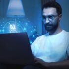 Homem moreno de barba e óculos olha para tela de computador