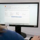 Mulher com cabelo claro está de frente para uma tela de computador no site da prefeitura