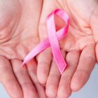 Palmas de mãos de uma mulher viradas para cima segurando um laço rosa