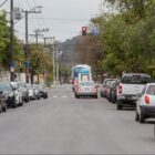 Rua com carros estacionados e outros parados em semáforo