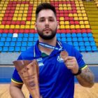 Atleta com camiseta azul segura medalha pendurada no pescoço