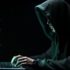 Homem com capuz acessa computador em ambiente escuro