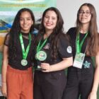 Três alunas jovens com medalhas posam para foto