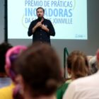 Secretário de saúde segura microfone e se dirige a plateia sentada em cadeiras na sua frente