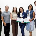 Seis pessoas posam para foto, duas mulheres seguram certificado