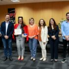 Nove pessoas, entre homens e mulheres, posam para foto. Uma mulher segura um certificado