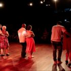 Casais dançam juntos em palco virados para plateia