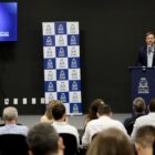 Prefeito discursa em púlpito de frente para plateia sentada