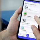 Mãos de um homem seguram celular e na tela está aberto o aplicativo da Prefeitura