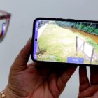 Mulher segura celular e acompanha imagens de câmera ao vivo