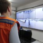 Dois agentes da Defesa Civil, um com colete laranja, observa situação de alagamentos em ruas em um grande telão
